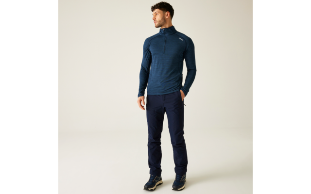 Ein Mann steht vor einem hellen Hintergrund, trägt ein dunkelblaues Langarmshirt und dunkelblaue Hosen