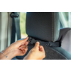 Two hands fasten a black strap with a plastic buckle around a car seat headrest