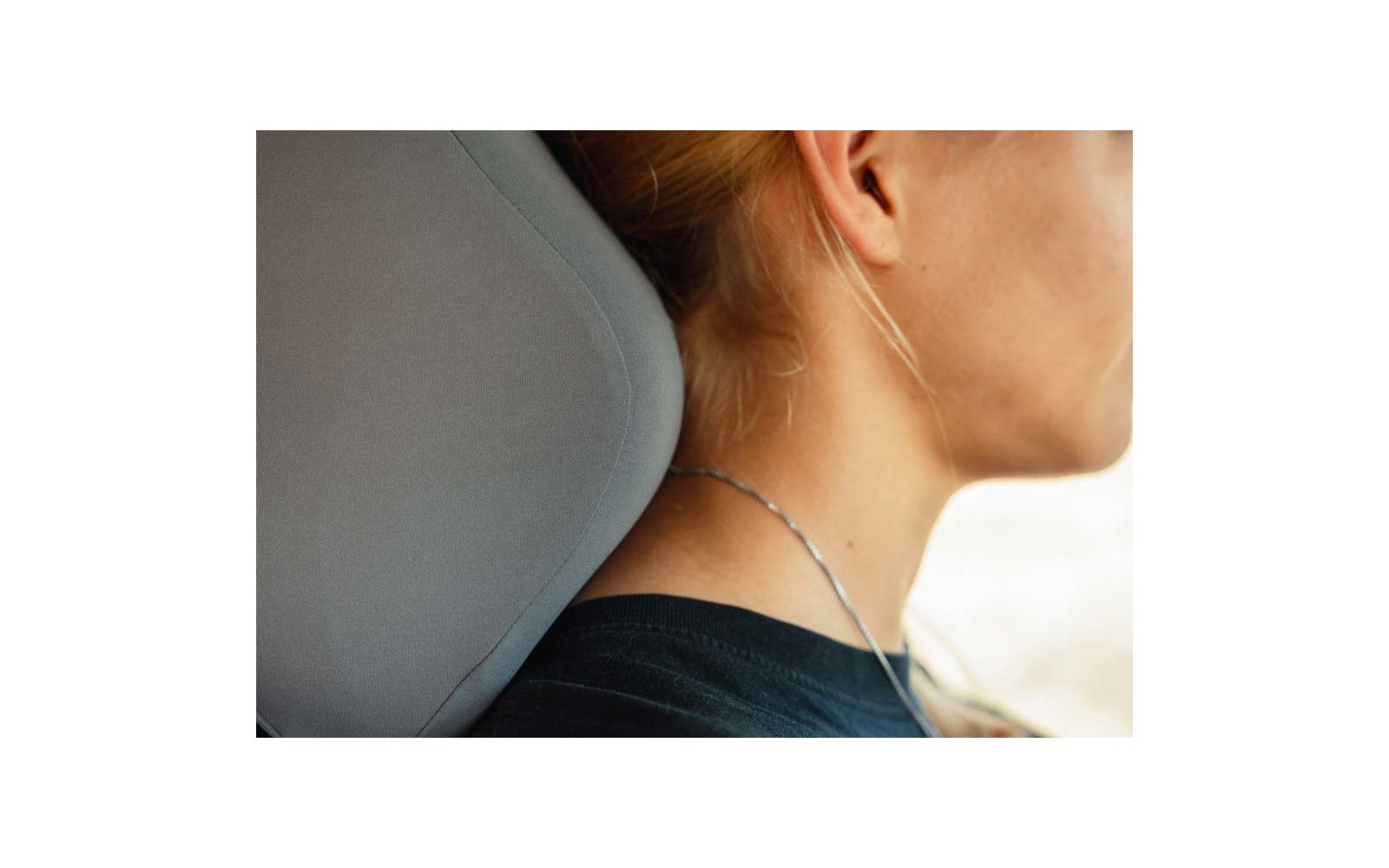 Side view of a person's neck with hair tied up, silver necklace, ear, black top and gray car headrest