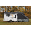 White motorhome on grass, front half covered with grey and black protective cover, window, door and wheel visible, trees with autumn foliage in the background