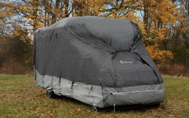 Housse de protection grise recouvrant un véhicule sur l'herbe, arbres aux feuilles d'automne en arrière-plan