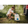 A person kneeling on grass next to a white water container with a blue cap and yellow handle, beside a parked van