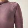 Oberkörper einer Person in eng anliegendem mauvefarbenem Langarm-Oberteil mit kurzem Stehkragen, sichtbarem Vorderreißverschluss und kleinem hellgrauen Logo links auf der Brust; heller Hintergrund