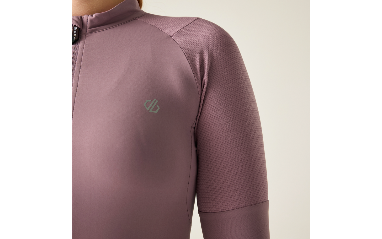 Oberkörper einer Person in eng anliegendem mauvefarbenem Langarm-Oberteil mit kurzem Stehkragen, sichtbarem Vorderreißverschluss und kleinem hellgrauen Logo links auf der Brust; heller Hintergrund