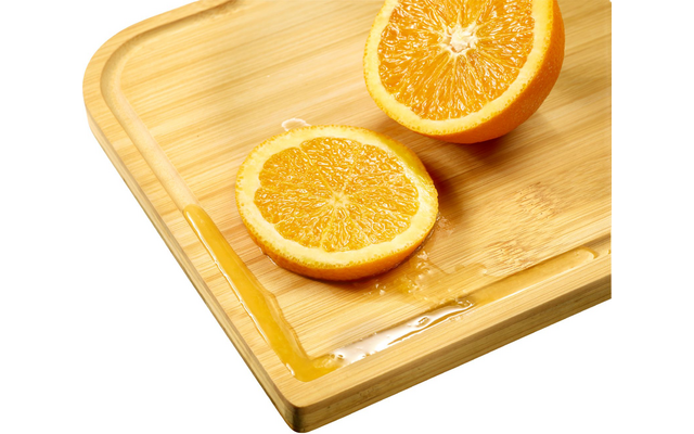 Two orange halves on a bamboo cutting board, juice on the board