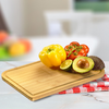 Wooden cutting board with a yellow bell pepper, vine tomatoes, a halved avocado with pit, and a lime half on a red-and-white checkered cloth