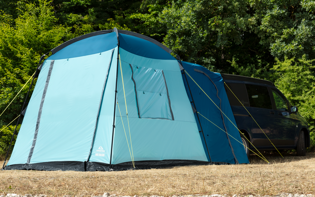 Tienda azul sobre hierba seca con árboles al fondo y un coche negro al lado