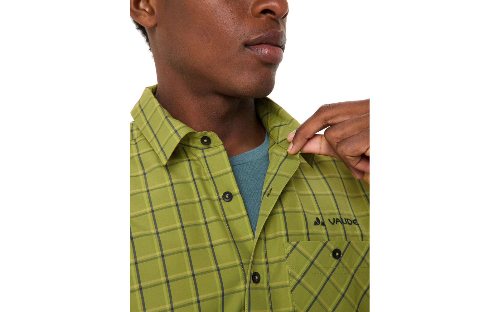 Nahaufnahme des Oberkörpers einer Person: Mund und Kinn sichtbar, rechte Hand hält den Kragen eines grünen karierten Hemds mit Brusttasche und schwarzem 'VAUDE'-Schriftzug, darunter blaugrünes T-Shirt