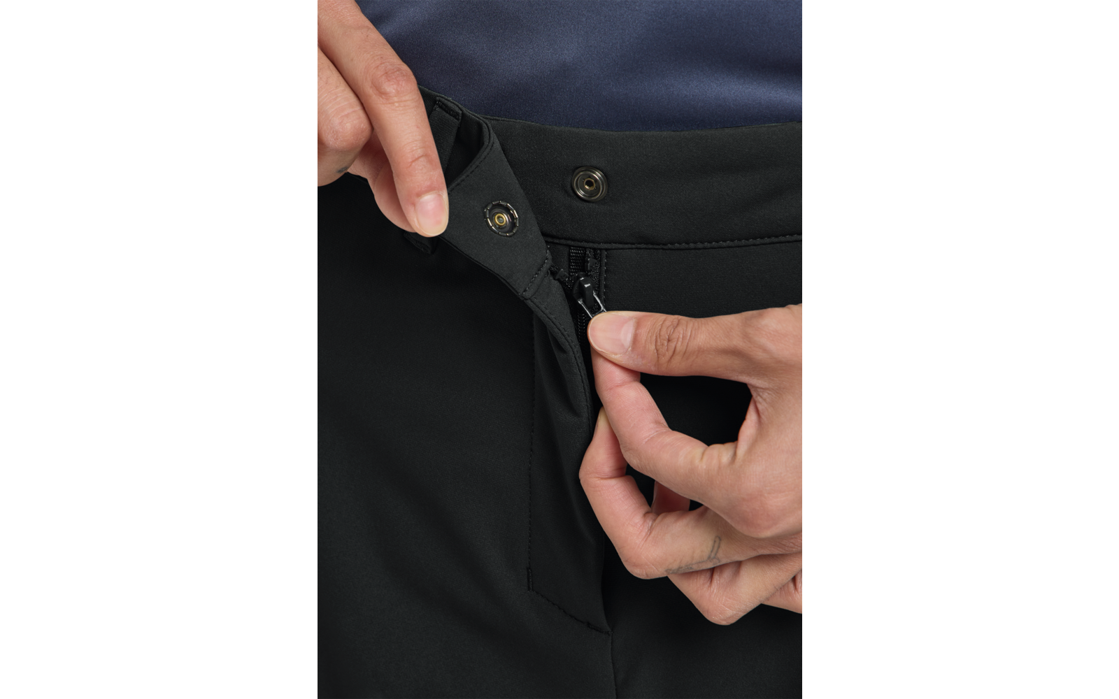 Zwei Hände schließen Reißverschluss und Druckknopf an der Taille einer schwarzen Hose; darüber ein dunkelblaues Kleidungsstück