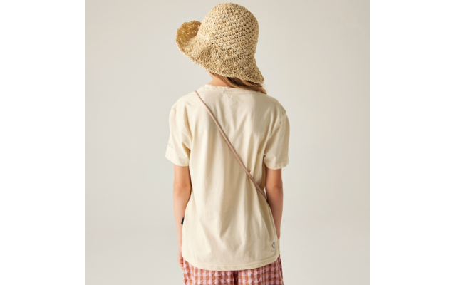 Person von hinten, trägt Strohhut, beige T‑Shirt, karierte Shorts und einen Trageriemen über dem Rücken