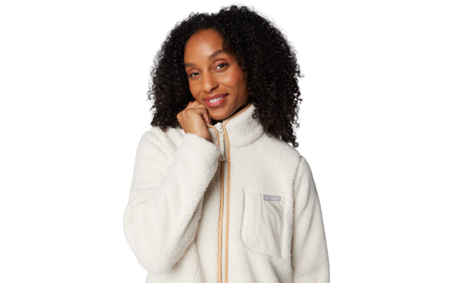 Nahaufnahme einer Person mit lockigem dunklem Haar, die eine weiße Fleecejacke mit Reißverschluss und Brusttasche trägt; eine Hand berührt das Kinn; weißer Hintergrund