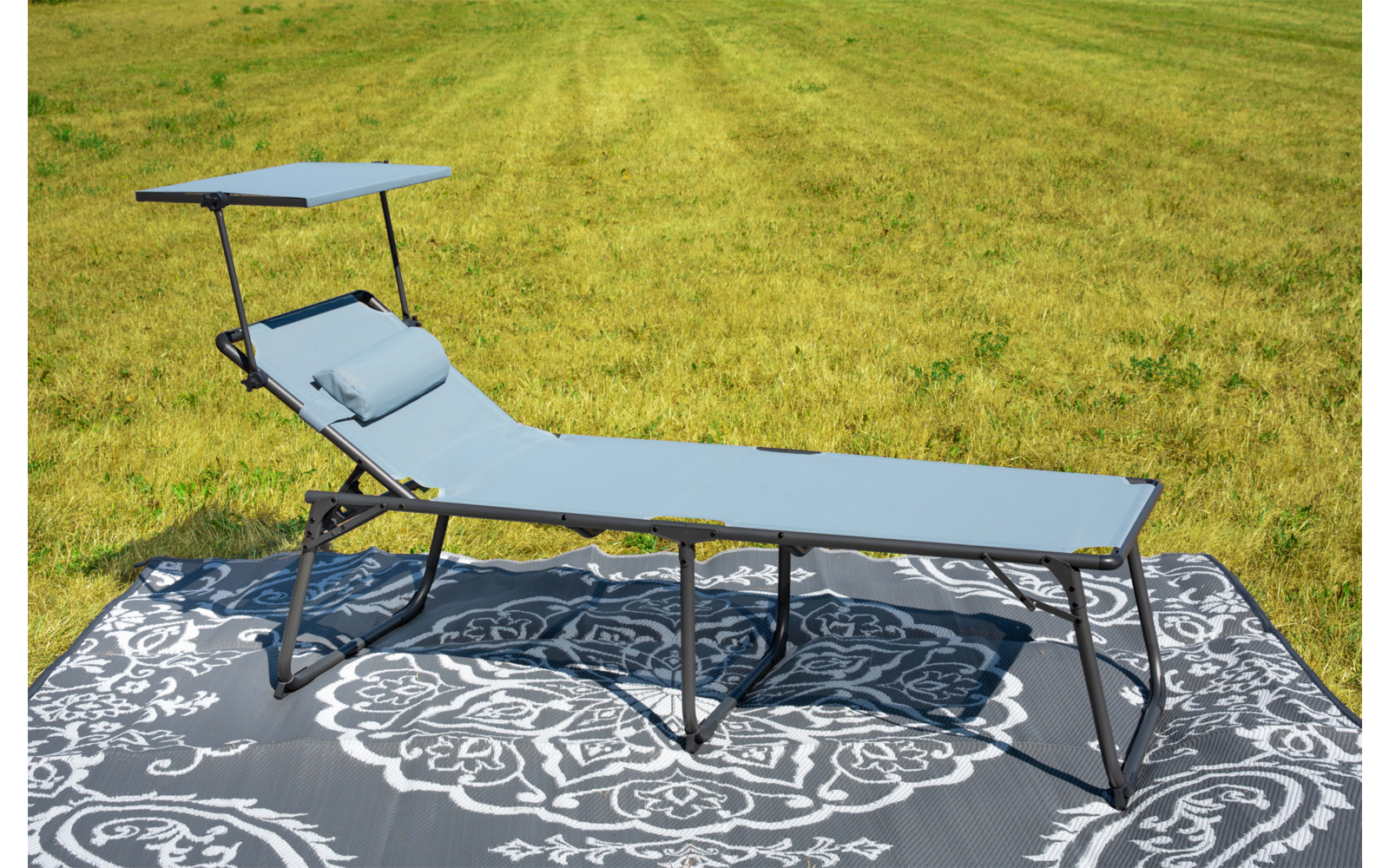 Lettino prendisole grigio-blu con cuscino su tappeto grigio a motivo bianco su prato verde