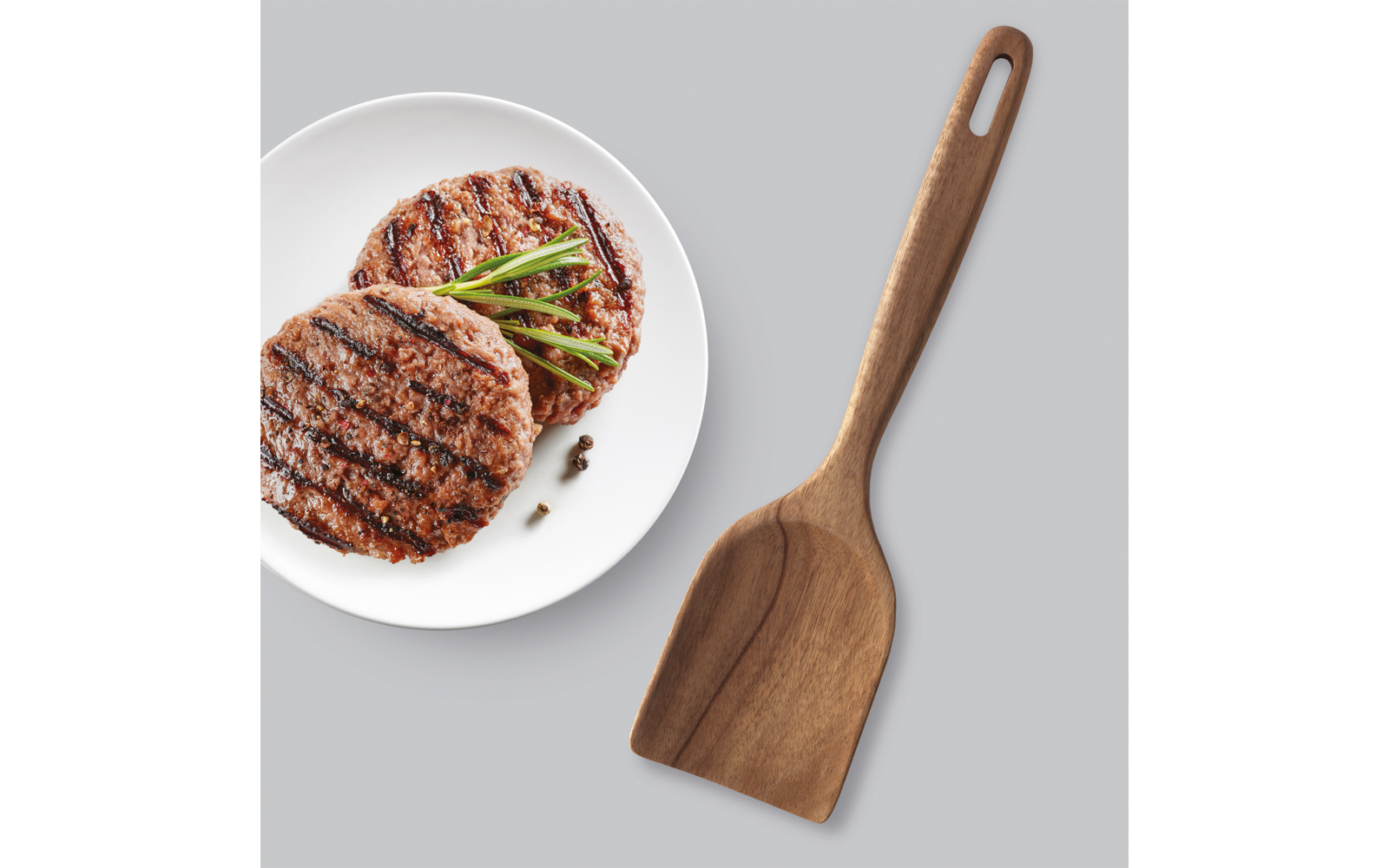Gegrillte Frikadellen auf einem weißen Teller neben einem Holzwender