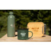 Grüne Trinkflasche, grüner Emaille-Becher mit Aufdruck „camp life“ und Holzbox mit Metallverschluss auf einem Holztisch, unscharfer grüner Hintergrund