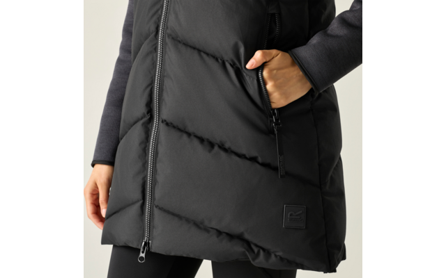 Tronco con piumino lungo nero imbottito con cerniera centrale; mano destra in tasca con zip; toppa quadrata visibile sull'orlo; maglia a maniche lunghe scura e leggings neri visibili