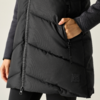 Tronco con piumino lungo nero imbottito con cerniera centrale; mano destra in tasca con zip; toppa quadrata visibile sull'orlo; maglia a maniche lunghe scura e leggings neri visibili