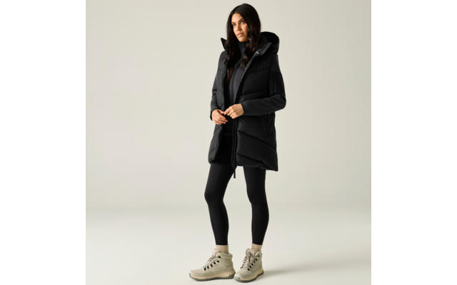 Donna in piedi su sfondo chiaro, indossa un gilet imbottito nero con cappuccio, top e leggings neri, stivaletti beige con lacci, mani davanti al corpo