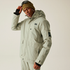 Person in hellgrauem Outdoor-Outfit mit beiger Mütze vor grauem Hintergrund