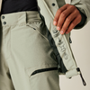 Nahaufnahme einer Person, die eine hellgraue Jacke mit Reißverschluss und Metallknöpfen trägt und die Jacke mit der rechten Hand hält