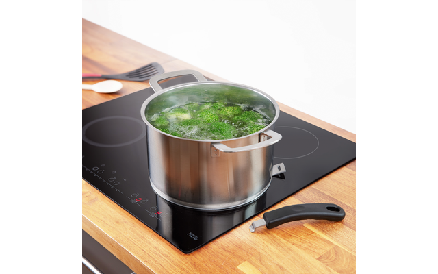 Casserole en acier inoxydable avec eau bouillante et morceaux de légumes verts sur une plaque à induction noire ; poignée amovible et ustensiles sur plan de travail en bois