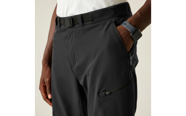 Zona de la cadera: pantalón oscuro con cinturón, una mano en el bolsillo, otra mano al costado, reloj en la muñeca, bolsillos con cremallera en el muslo, borde de camiseta blanca visible