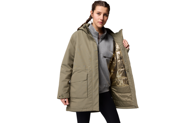 Mann trägt eine lange, beige Jacke und hält sie geöffnet, darunter graues Sweatshirt und schwarze Hose