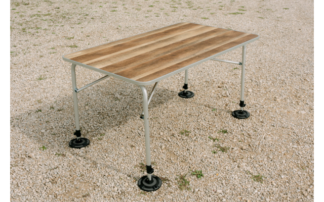 Table rectangulaire avec plateau en bois brun clair et quatre pieds métalliques gris clair munis de plaques de pied rondes noires, posée sur du gravier