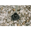 Objet rond noir sur une tige de couleur claire posé sur des cailloux blancs et gris