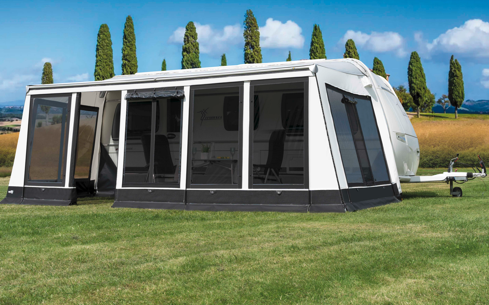 Witte caravanluifel op groen gras met bomen en blauwe lucht op de achtergrond