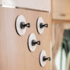 Four round white discs with black plastic hooks on a wooden panel