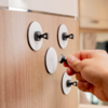 Right hand holds a small black round object against a light brown wood panel with four white round discs and black hooks