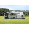 Wit-grijze caravan met aangebouwde grijze voortent op een groen veld, bomen en bewolkte lucht op de achtergrond