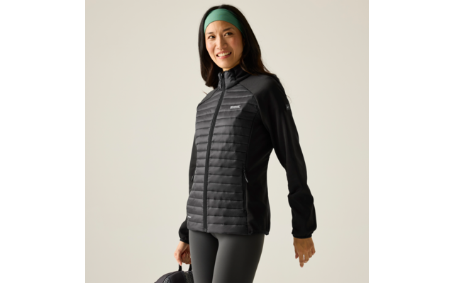 Persoon in driekwartsprofiel draagt een zwarte doorgestikte jas met rits, zwarte legging, een groen haarband en houdt een zwarte tas