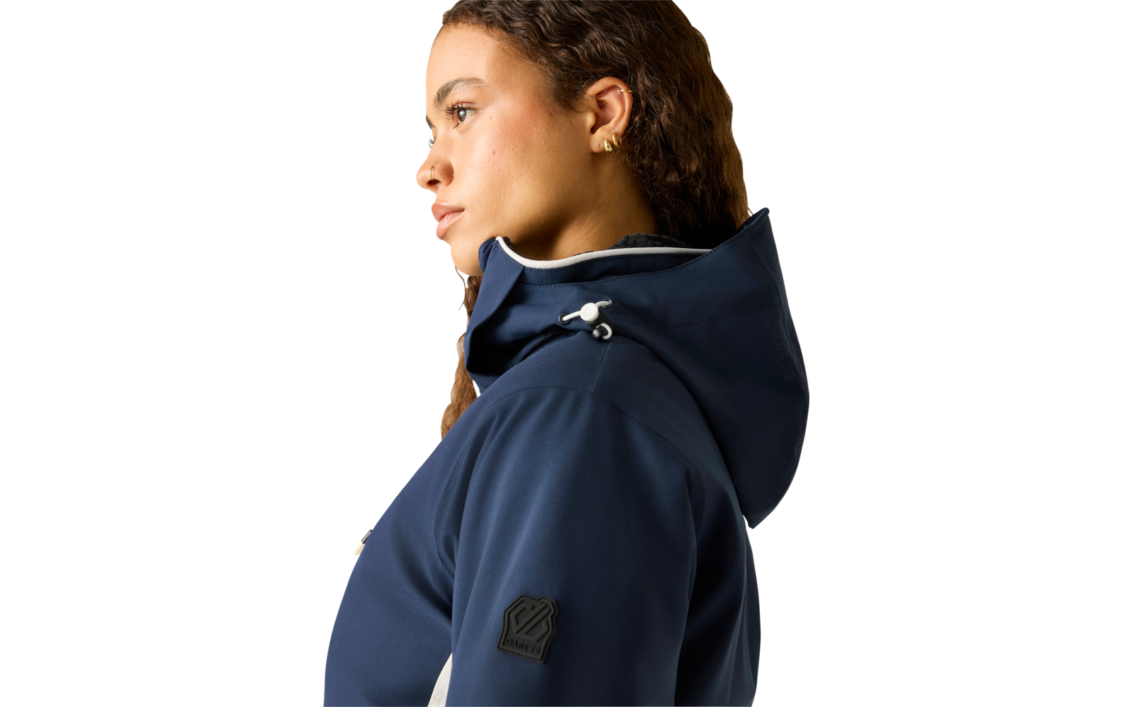 Seitliches Porträt einer Person mit lockigem braunem Haar, die eine dunkelblaue Kapuzenjacke mit Kordelzug und goldene Ohrstecker trägt