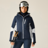 Person in dunkelblauer Skijacke mit weißen Einsätzen, trägt Helm und Skibrille, hält Skistöcke, steht frontal vor hellem Hintergrund