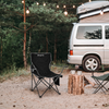 Campingplatz mit weißem Van, schwarzem Klappstuhl, Baumstümpfen und Lichterkette in Wäldern