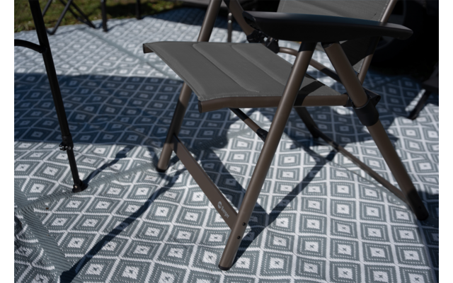 Klapphocker mit grauer Sitzfläche und braunen Beinen auf blau-weißer Unterlage mit Rautenmuster, Schatten der Hockerbeine