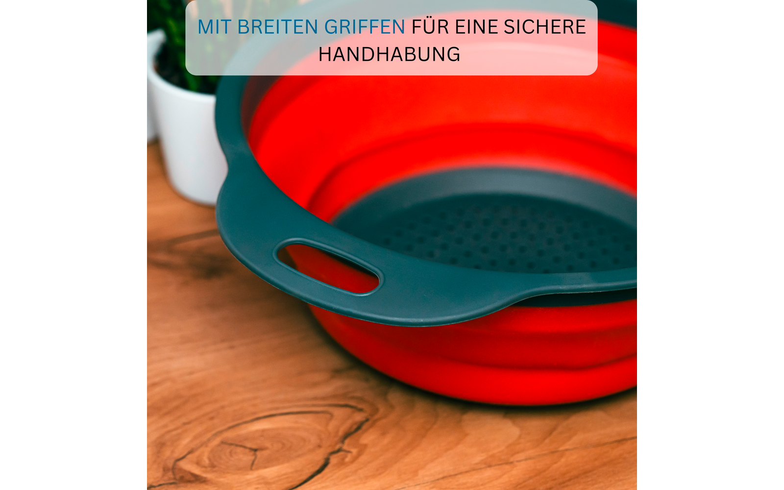 Rotes, faltbares Silikonsieb mit dunkelgrauen breiten Griffen und gelochtem Boden auf Holzuntergrund; links unscharfer weißer Blumentopf; oben transparente Textleiste mit der Aufschrift "MIT BREITEN GRIFFEN FÜR EINE SICHERE HANDHABUNG"