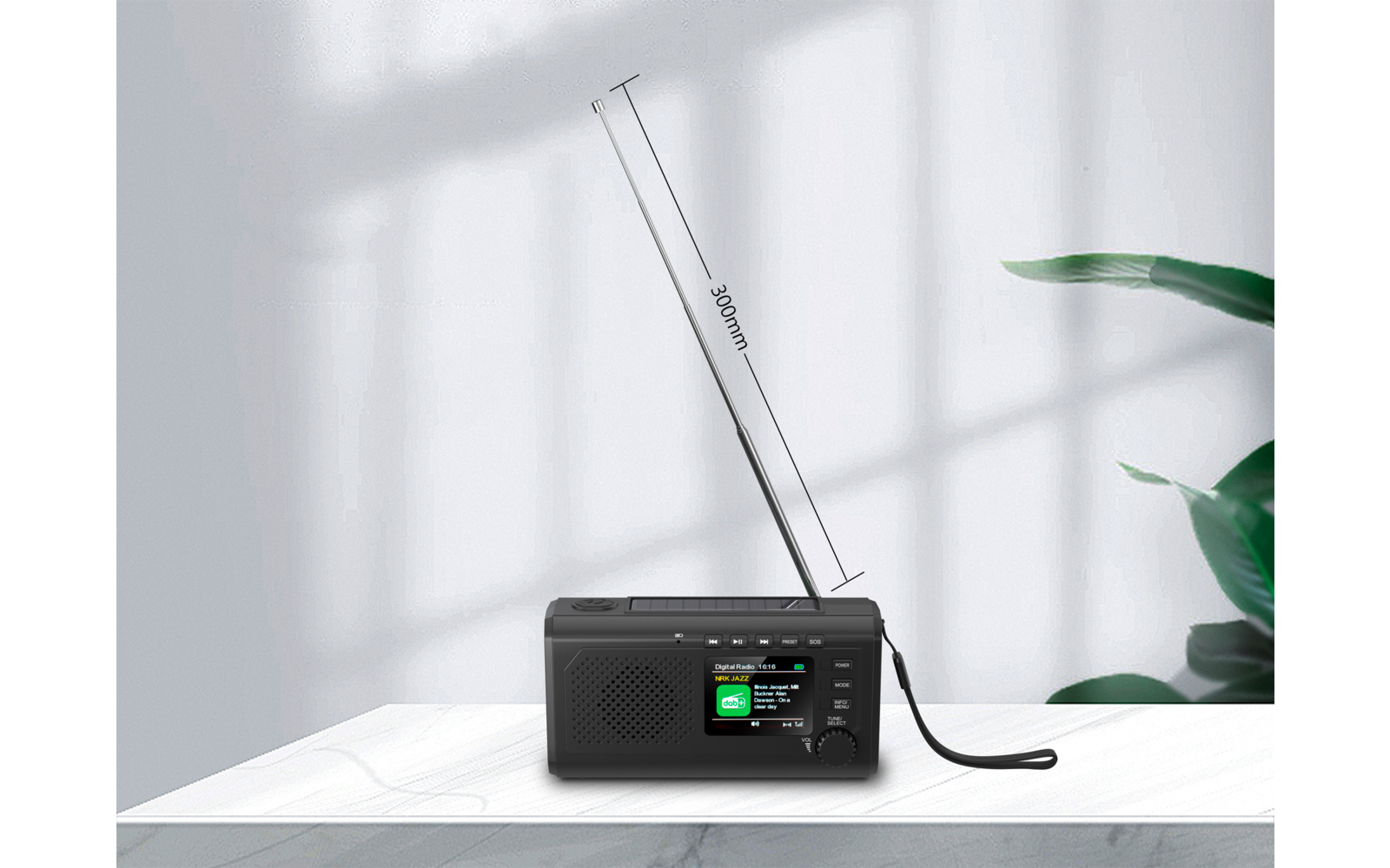 Schwarzes Radio auf weißem Tisch, ausgezogene Antenne mit Markierung "360mm", Lautsprechergitter, Display und Drehknopf; Fenstergitter-Schatten auf weißer Wand; rechts grüne Pflanze