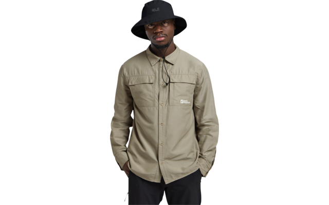 Person steht frontal, trägt schwarzen Anglerhut, beiges Hemd mit Brusttaschen und Logo, Hände in Hosentaschen