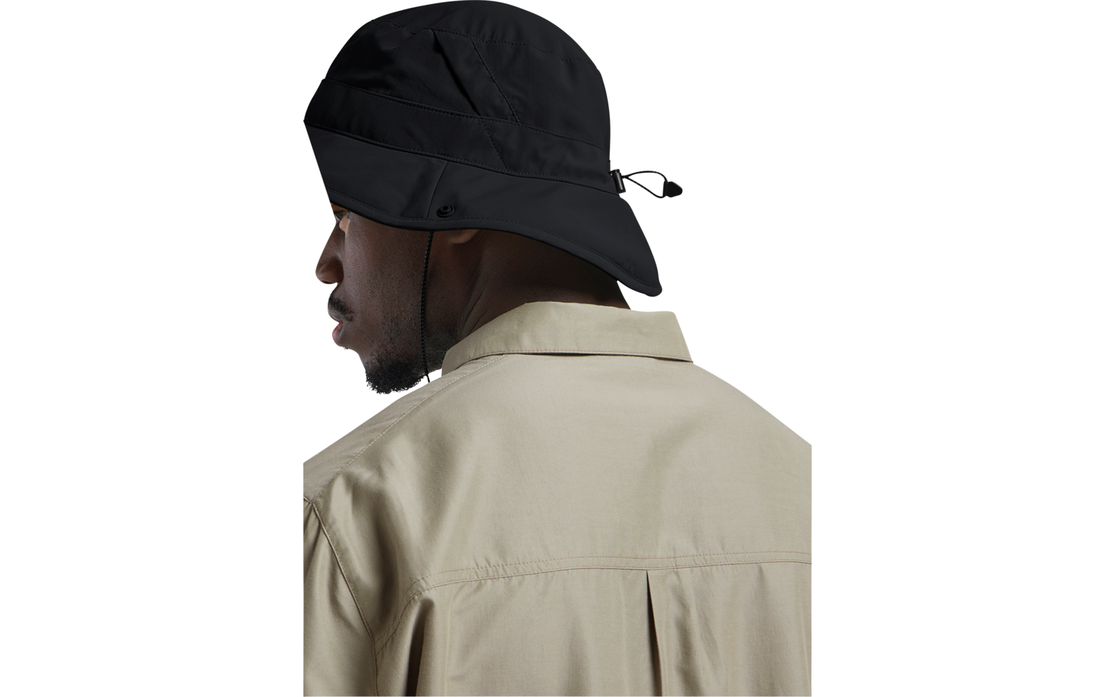 Person im Halbprofil von hinten, trägt schwarzen Anglerhut mit Kinnriemen und hellbeige Jacke mit Rückenfalte