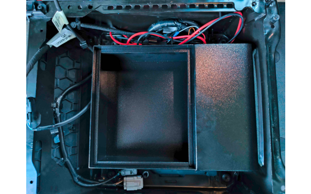 Carcasa de dispositivo abierta con un compartimento metálico cuadrado vacío en el centro, cables rojos y negros visibles, conectores y bordes de la carcasa