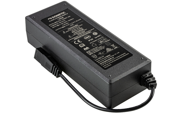 Schwarzes, rechteckiges Gehäuse mit schwarzem Aufkleber mit technischem Text und Symbolen; an einem Ende befestigtes schwarzes Kabel mit rechteckigem Stecker