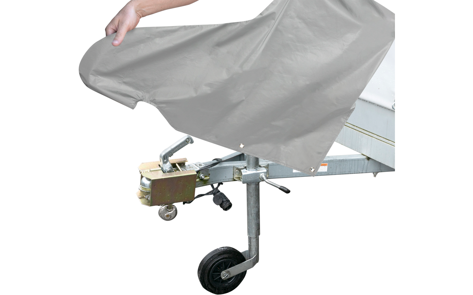 Hand zieht eine graue Abdeckung über den vorderen Bereich eines Anhängers; sichtbare Metallkupplung, Zugmaul, Stützrad und Rahmen