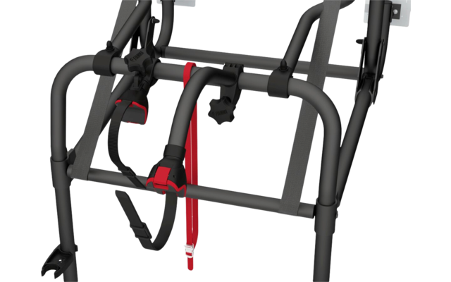 Nahaufnahme eines grauen Metallrahmens mit schwarzen Kunststoffverbindungen, grauen Textilgurtbändern, einem schwarzen Drehknopf und einem roten Riemen mit Metallschnalle