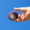 Hand hält ein Glas mit dunkler Flüssigkeit vor blauem Himmel