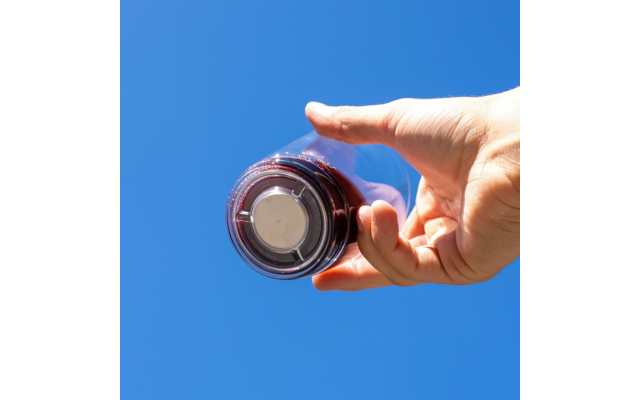 Hand hält ein Glas mit dunkler Flüssigkeit vor blauem Himmel