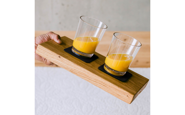 Hand hält ein Holzbrett mit zwei Gläsern Orangensaft