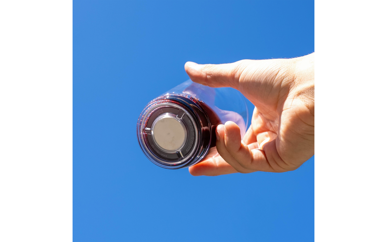 Hand hält eine durchsichtige Plastikflasche mit dunklem Getränk vor blauem Himmel