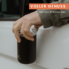 Hand hält einen schwarzen Becher mit transparentem Deckel vor einer weißen Autotür; oben ein rotes Banner mit dem Schriftzug "VOLLER GENUSS" und darunter kleiner weißer Text "frei von BPA und Blei"
